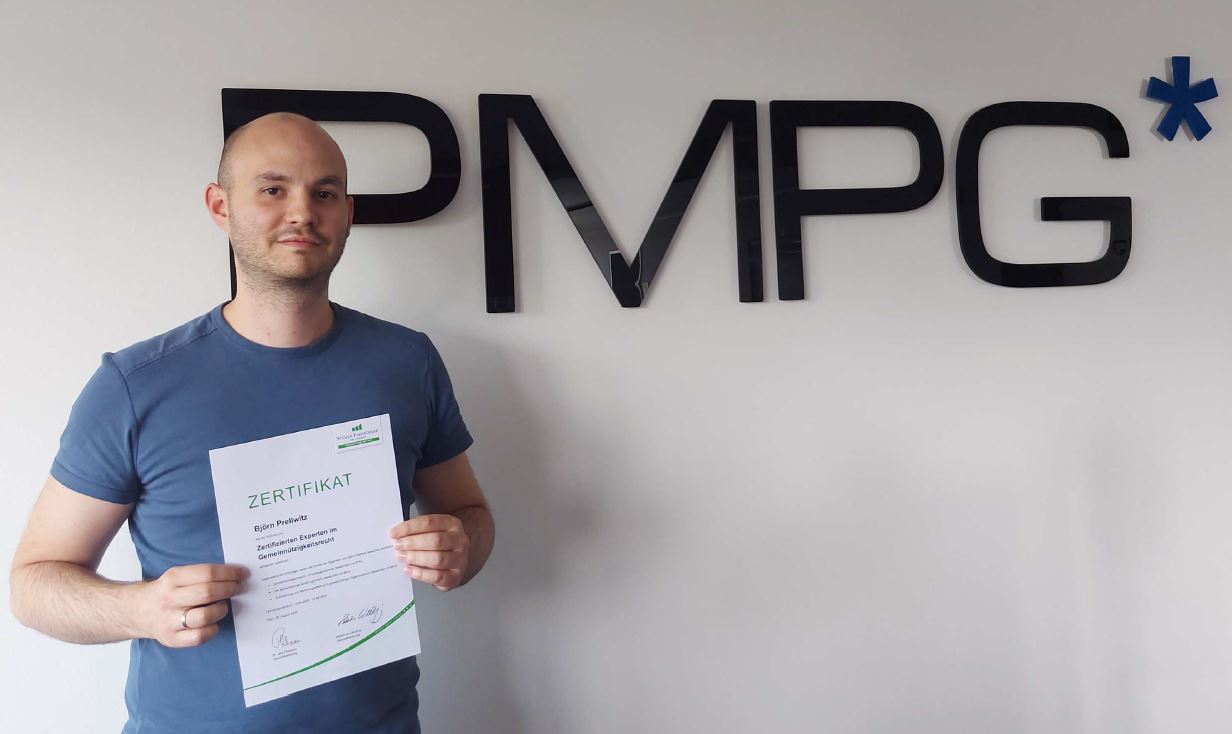 PMPG-Mitarbeiter Bjoern Prellwitz steht mit dem Zertifikat zum Zertifizierten Experten für Gemeinnützigkeitsrecht vor einer Wand mit PMPG-Logo