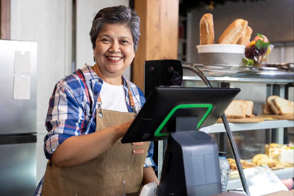 Lächelnde, altere Dame hinter Bäckereitresen, an Kasse