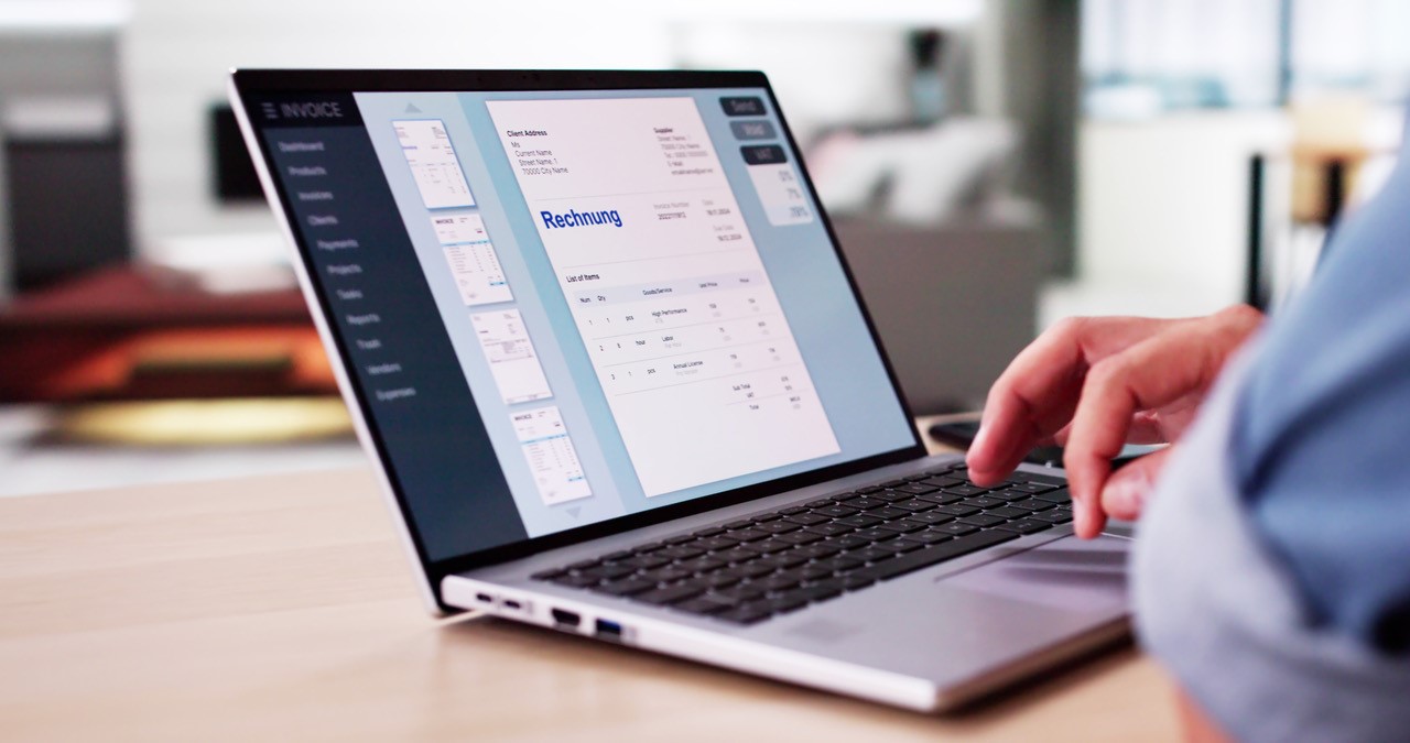 Laptop mit einer Rechnung auf dem Bildschirm, angeschnittene Person sitzt vor dem Bildschirm